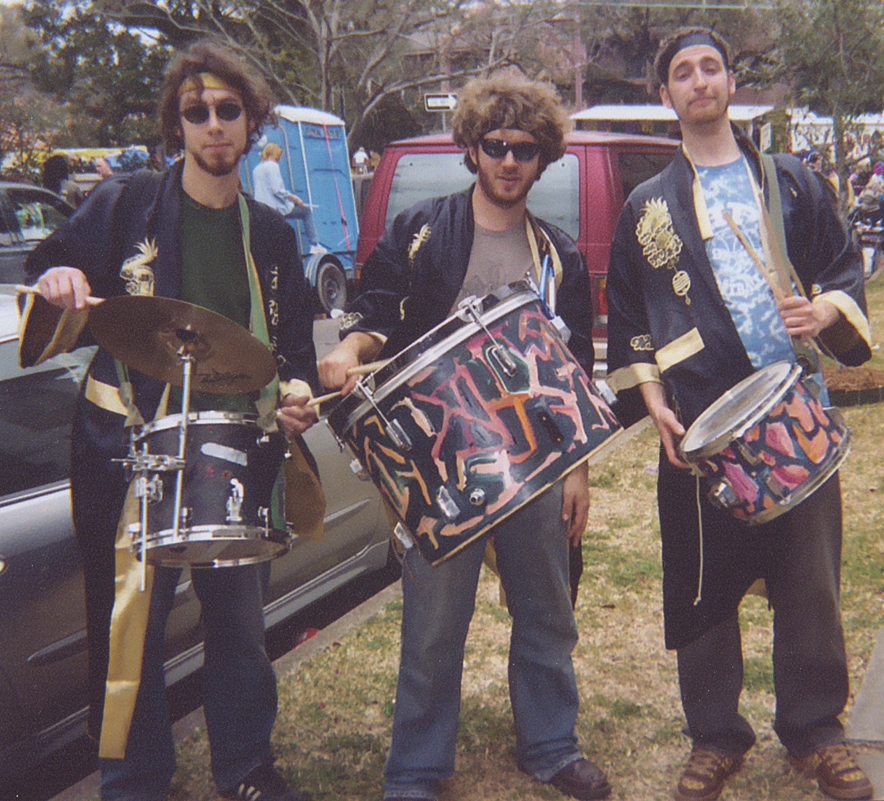 The three members of WAW at Mardi Gras in black robes, carrying painted marching drums